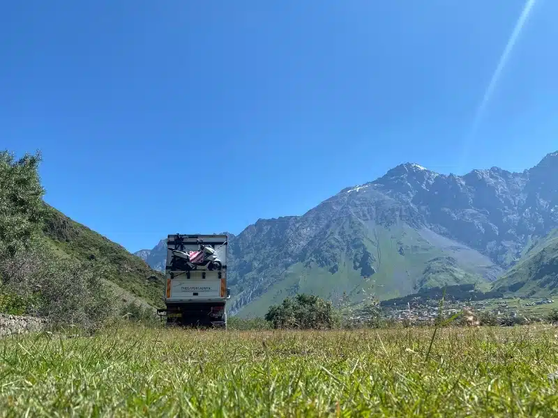 white overland truck parked ona. grassy meadow with a mountain backdrop