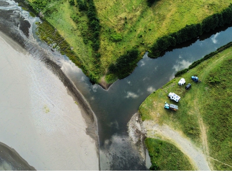motorhomes parked in a grassy field by a wide river