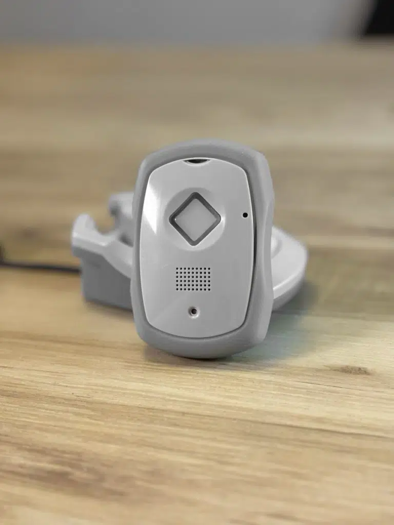 A portable GPS medical alert device with SOS button and charging cradle on a wooden surface
