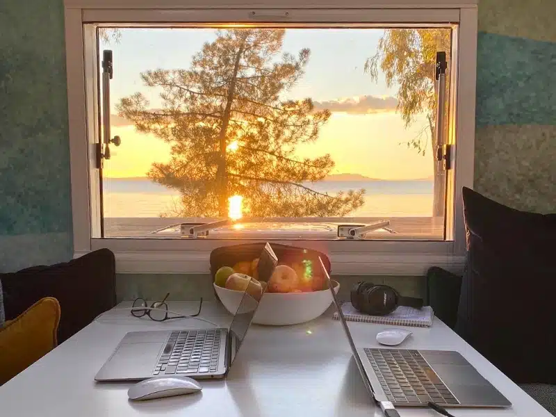 Two laptops on a campervan table with a view of the sunset