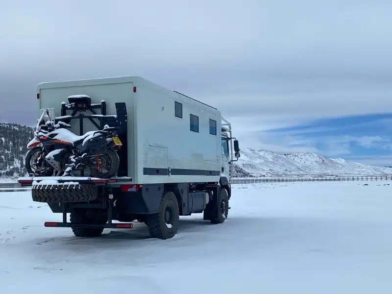Overland truck camper parked in snow by an icy lake