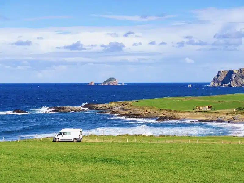 Camper van in a grassy field by a rocky shoreline