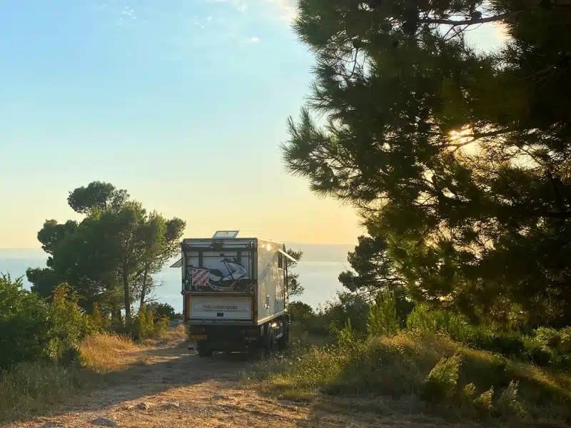 camper truck parking on a sandy track with an ocean view and surrounded by pine trees
