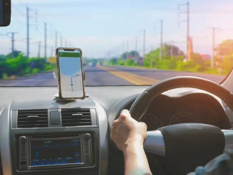 Car Driver using Smartphone with GPS Map Navigation App while Driving on the Road,