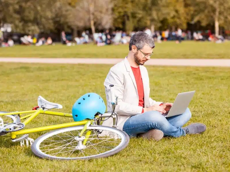 Professional man working with laptop computer at a park with bike next to him