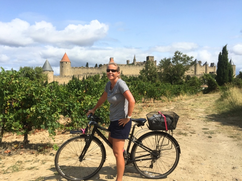 woman on a bike in a grove of trees with a castle behind