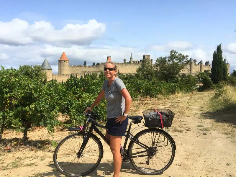 woman on a bike in a grove of trees with a castle behind