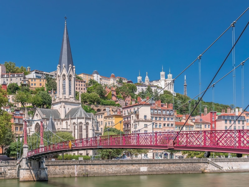 Saint George Church, Quais de Saone, and Fourviere Basilica from a footbridge in Vieux Lyon, France, showcasing historic architecture, reflections and a scenic river view