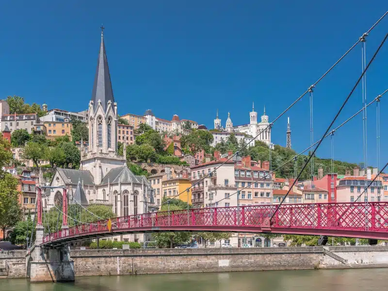 Saint George Church, Quais de Saone, and Fourviere Basilica from a footbridge in Vieux Lyon, France, showcasing historic architecture, reflections and a scenic river view