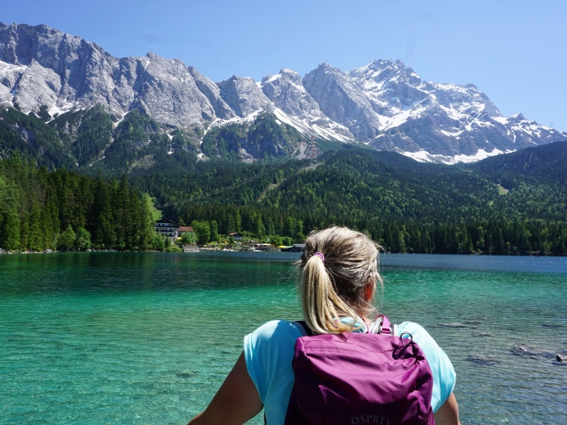 Woman with pink rucksack looking across the turquoise water of a lake to a snow capped mountain range
