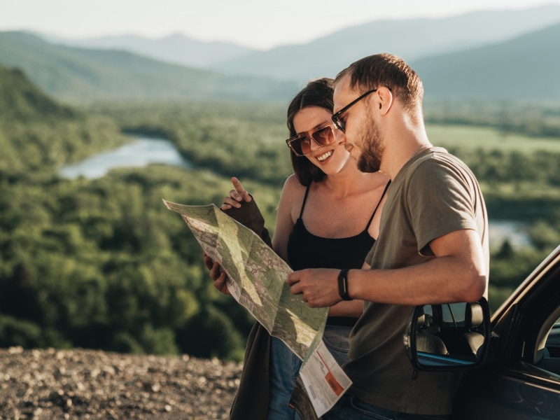 Travelers Couple on Road Trip, Man and Woman Using Map on Journey Near Their Car Over Beautiful Landscape