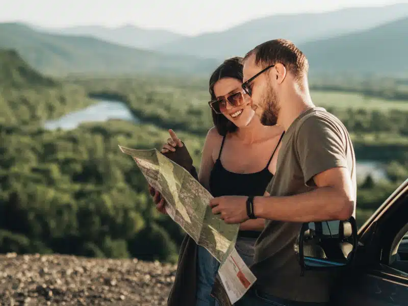Travelers Couple on Road Trip, Man and Woman Using Map on Journey Near Their Car Over Beautiful Landscape