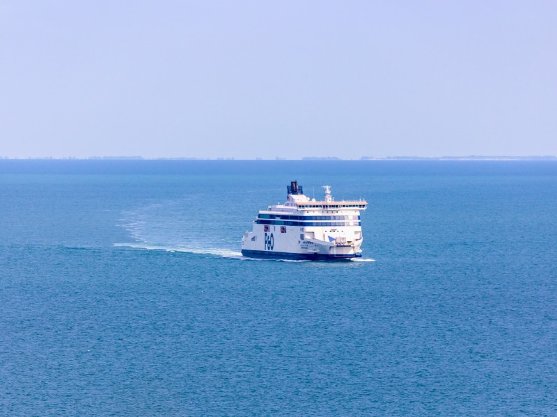 Passenger ferry crossing the calm blue sea between England and France on a hazy day.