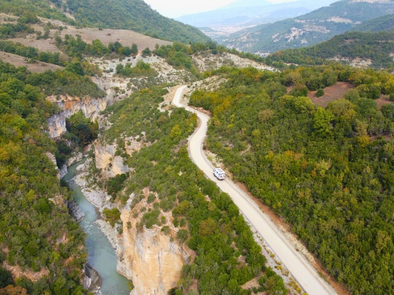 white truck on a road by a deep river canyon with mountains in the distance